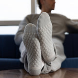 A person reclining on a blue couch with their legs raised, wearing light gray textured knit socks and matching lounge pants in a bright indoor setting.
