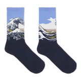 A pair of crew socks featuring a graphic print of Katsushika Hokusai's Great Wave off Kanagawa. The lower half of the socks is a solid dark navy blue, while the upper half features the wave illustration with a light blue sky, white foam, and a tan mountain range.