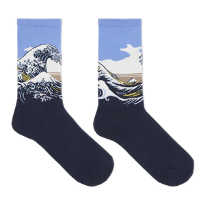 A pair of crew socks featuring a graphic print of Katsushika Hokusai's Great Wave off Kanagawa. The lower half of the socks is a solid dark navy blue, while the upper half features the wave illustration with a light blue sky, white foam, and a tan mountain range.