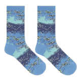 A pair of crew socks with a detailed watercolor-style print of a lake or river scene, featuring blue and light teal water, white ripples, and green reeds, displayed against a solid white background.