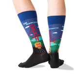 A pair of crew socks worn on feet, featuring a colorful San Francisco-themed graphic with the Golden Gate Bridge, trolleybus, and 'SAN FRANCISCO' text on a white background.