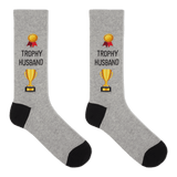 A pair of heather gray crew socks with black heels and toes, featuring a gold trophy graphic and the text 'TROPHY HUSBAND' printed on the front. thumbnail