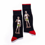 A pair of black crew socks with red cuffs, heels, and toes, featuring a graphic print of Michelangelo's David statue with a green bow-tie overlay. thumbnail