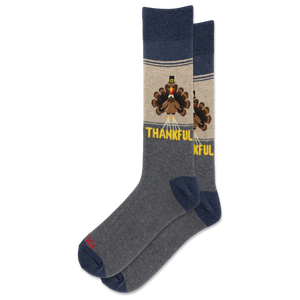 A pair of crew socks with a Thanksgiving theme. The socks feature a heather gray body, navy blue heels and toes, and a beige upper section with a cartoon turkey graphic and the word 'THANKFUL' in yellow.