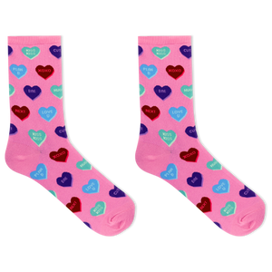 A pair of pink crew socks with an all-over pattern of colorful heart candies in red, blue, purple, and green, each printed with Valentine's themed phrases like 'Kiss Kiss', 'Love You', and 'HUGS'.