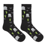 A pair of black crew socks with a Halloween-themed print featuring green zombie hands, gray tombstones, and gray bats, displayed against a solid white background.
