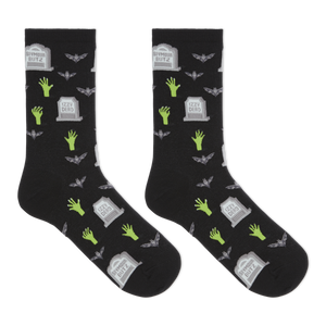 A pair of black crew socks with a Halloween-themed print featuring green zombie hands, gray tombstones, and gray bats, displayed against a solid white background.