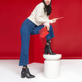 Woman sitting on a white stool against a red background, holding a red box.