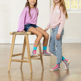 Two children wearing colorful socks and standing on a wooden floor. thumbnail