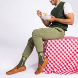 Man sitting on a red and white checkered tablecloth, wearing green socks with pasta print. thumbnail
