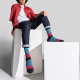 A model wearing colorful striped crew socks, a red button-up shirt, and dark jeans sits on white geometric display blocks against a light gray studio background. thumbnail