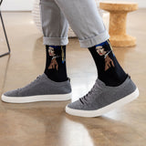 A person wearing black crew socks with a graphic print of 'Girl With a Pearl Earring' and gray knit sneakers, standing on a polished wood floor.