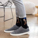 A person wearing black crew socks with a graphic print of 'Girl With a Pearl Earring' and gray knit sneakers, standing on a polished wood floor.
