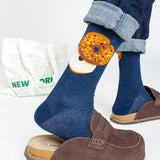 Person wearing blue socks with a bagel design, paired with brown shoes and a white bag with 'New York' text.