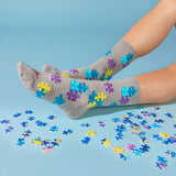 A pair of gray crew socks with colorful jigsaw puzzle-piece patterns, worn on feet with scattered puzzle pieces on a light blue background. thumbnail