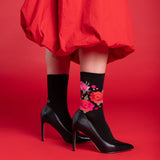 Person wearing black high-heeled shoes and floral socks on a red background