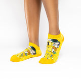 A pair of low-cut yellow socks with a Gustav Klimt 'The Kiss' art print, shown on a model's feet against a white background.