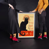 Two people holding a framed poster of a black cat with a dark background