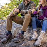 Two people sitting on rocks outdoors, wearing hiking shoes and enjoying a snack. thumbnail