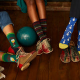 Three people wearing colorful socks and shoes with a bowling ball on a wooden floor. thumbnail