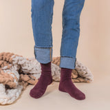 Person wearing maroon velvet socks with rolled-up blue jeans against a beige background thumbnail