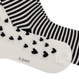 Two pairs of socks from k.bell, one in black and white stripes and the other in off-white with black hearts, shown on a white background.
