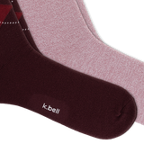 Two pairs of crew socks from k.bell, featuring a dusty rose pair, and a red and navy argyle pattern on a dark burgundy pair, arranged diagonally on a white background.