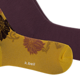A close-up of two socks from k.bell, featuring a metallic gold sock with a floral pattern and white brand text, layered over a solid dark plum purple sock, on a white background. thumbnail