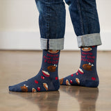 Person wearing blue socks with Thanksgiving-themed design and rolled-up jeans on a light wooden floor.