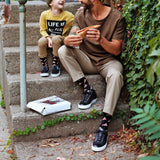 Man and child sitting on steps eating pizza, surrounded by greenery.