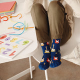 Child wearing blue socks with guitar design sitting on a chair next to a table with colorful letters.