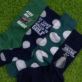 Four pairs of socks with humorous golf-themed designs on a grass background thumbnail