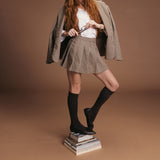 Person wearing a plaid skirt and jacket with brown knee-high socks and shoes on a brown background thumbnail