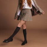 Person wearing a plaid jacket, white shirt, brown skirt, brown shoes, and brown socks on a brown background thumbnail