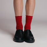 Red socks with white cuffs worn with black shoes on a neutral background