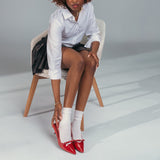 Woman sitting on a chair wearing a white shirt, black skirt, white socks, and red high heels.