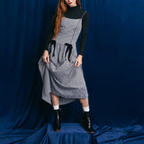 Person wearing a gray checkered dress with black accents against a blue backdrop